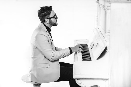 Cheerful young man in stylish suit is playing piano