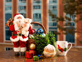 Santa Claus and Christmas tree decorations on the background of the windows. Tea and dessert for breakfast at the New Year's morning. On the mug of tea image symbol of the new year a fiery rooster.