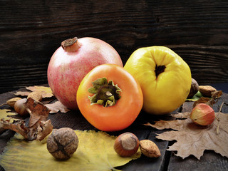 Autumn harvest. Persimmon, quince, pomegranate and yellow leaves on the wooden table