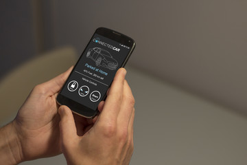 Hands holding mobile phone with connected smart car app on the screen.