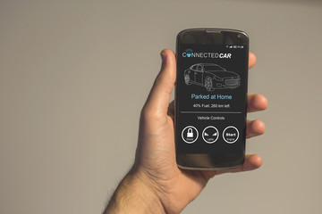 Hand holding smartphone with connected smart car app on the screen.