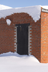 Locked shut metal door covered with snow. Brick wall building.