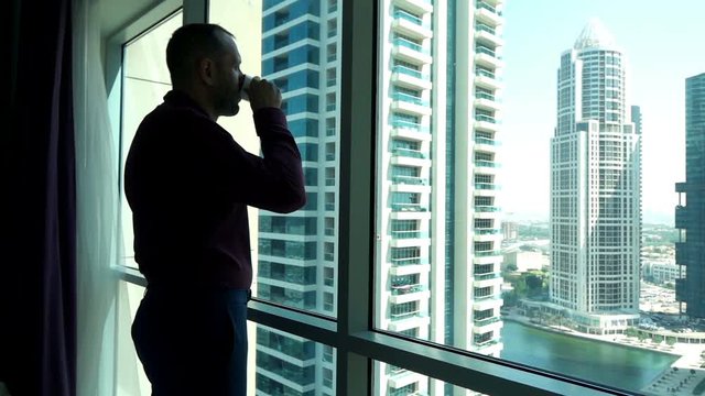 Young businessman drinking coffee and looking through tke window, super slow motion 
