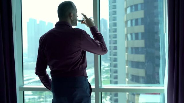 Young businessman drinking red wine and looking through tke window, 4K 
