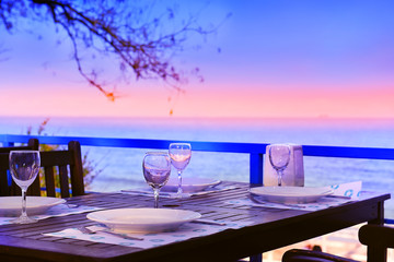 served table on the sea shore. glasses, plates, coasters saucer on brown wooden table. In the background, the sea and the light of the setting sun, sunset. Pleasant warm evening, 

