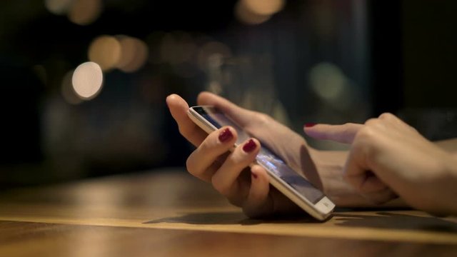Woman browsing photos on smartphone sitting by table at home at night
