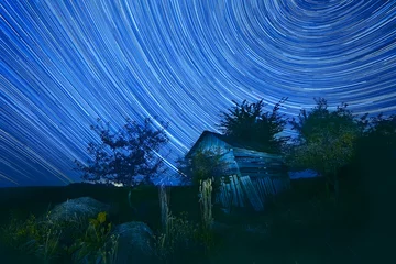 Foto auf Acrylglas night photography sky star tracks on the background of an old wooden barn housing. Rural wilderness.   © Ann Stryzhekin