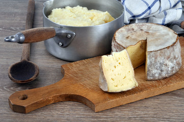 Tomme de Savoie sur une planche à découper avec une casserole d'aligot