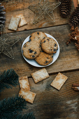 Chocolate cookies in a white plate on wooden background. Near cones and cinnamon stick, roughly. View from above. The theme of the new year holiday