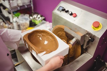 Mid section of worker filling mould with melted chocolate