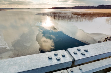 HDR photo of melt water behind metallic bridge railings at a freezing lake