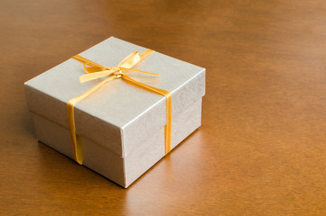 Silver gift box with golden ribbon on wooden background