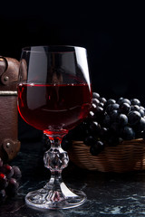 Glass of red wine on dark marble background. Cluster of blue gra