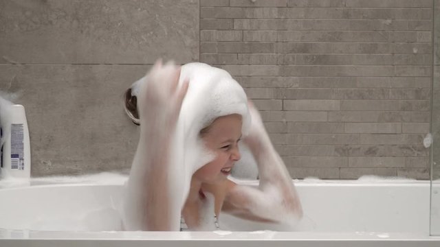 Little girl fooling with foam, making a hat  in the bathroom