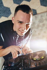 Young man DJ with headphones is working on turntable console mixer controlling