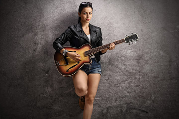 Fototapeta premium Young woman playing a guitar and leaning on a rusty gray wall