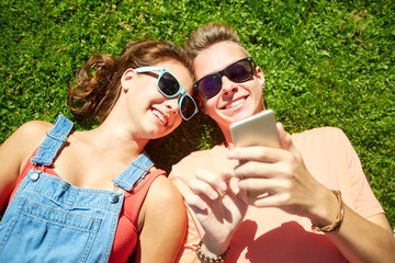 happy teenage couple smartphone lying on grass