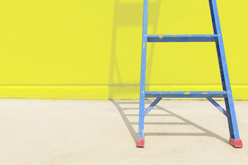 The blue steel ladder with the yellow concrete  wall