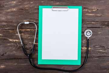 Medical clipboard and stethoscope on dark wooden table.