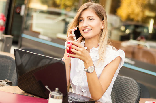 Young beauty smiling woman sitting in a cafe and talking on the cellphone