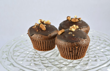 three chocolate brown muffins with nuts on glass plate detail