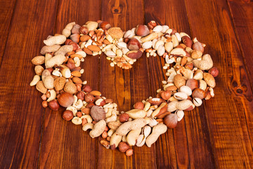 Various nuts stacked in shape heart on background dark wood.