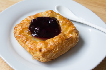 Danish blueberry pie with spoon in white plate on wooden table