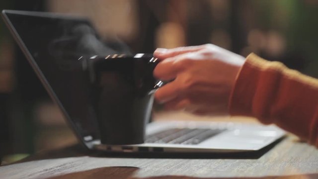 Still footage of a person typing on a computer and grabbing a steamy coffee mug.