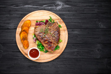 Grilled T-Bone Steak with seasoning and sauce on black wooden ba