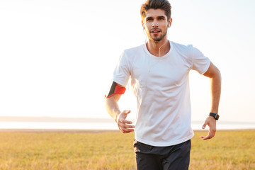 Fototapeta premium Handsome young sportsman running outdoors and listening to music