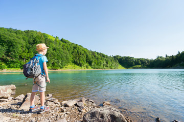 Small boy in hat and with backpack  on the beautiful mountain  lake. Travel concept.