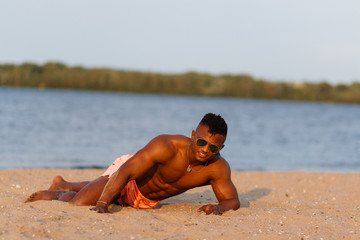 Fototapeta na wymiar Muscular young athletic sexy man on the beach with a naked torso in underwear. Hot black beautiful guy, fitness model with a rangy sports body.