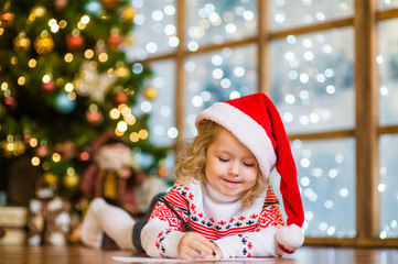 Little girl in Santa hat writes letter to Santa Claus