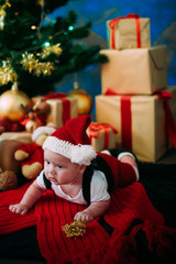 Fototapeta na wymiar fairy-tale portrait of Christmas cute little baby wearing like santa claus at the new year background under tree