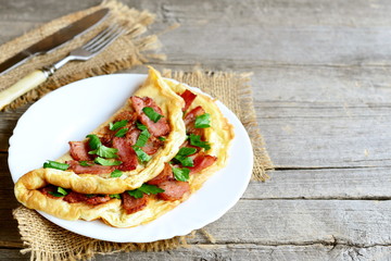 Fried egg omelet. Tasty omelet with fried bacon and fresh parsley on a plate, fork, knife on old wooden background with copy space for text. Delicious breakfast menu. Rustic style 