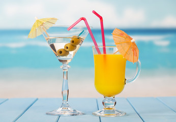 Glass orange juice and alcohol with olives on background sea.