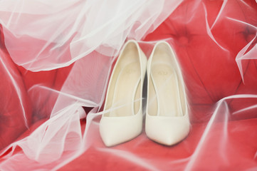 Белые туфли невесты под вуалью на красном диване