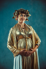 Pregnant woman in golden toga and wreath posing like a Greece fertility goddess