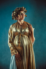 Pregnant woman in golden toga and wreath posing like a Greece fertility goddess