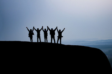silhouette group people hold hands together on the top of the mountain