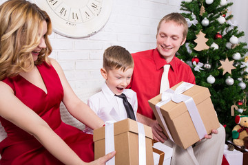 parents giving presents to their son in front of Christmas tree