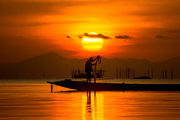 silhouette of fishermen with sunset sky on the lake.