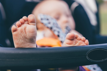 Baby sitting and playing with a toy in navy pram stroller with focus on feet and toes