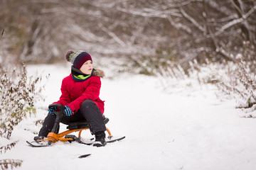 Fototapeta na wymiar Portrait of cute kid boy sitting on sledge on the snow on a winter day. Child playing outdoors. Lifestyle concept