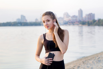 Fototapeta premium Young girl at river listening to music on cell phone