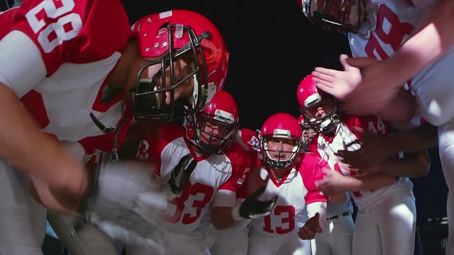 The camera looks up into a huddle full of football players talking before a play