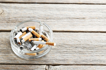 Cigarette butts with ash in ashtray on grey wooden table