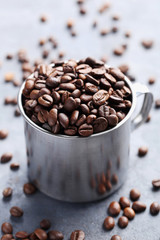 Roasted coffee beans in mug on grey table