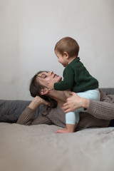 young mother and baby in  knit sweaters playing on  bed, concept