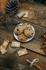Fototapeta premium Chocolate cookies in a white plate on wooden background. Near cones and cinnamon stick, roughly. View from above. The theme of the new year holiday